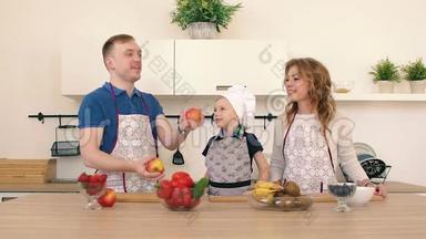 一家人正在厨房准备沙拉.. 爸爸把苹果扔了起来。 儿子和他母亲在微笑。